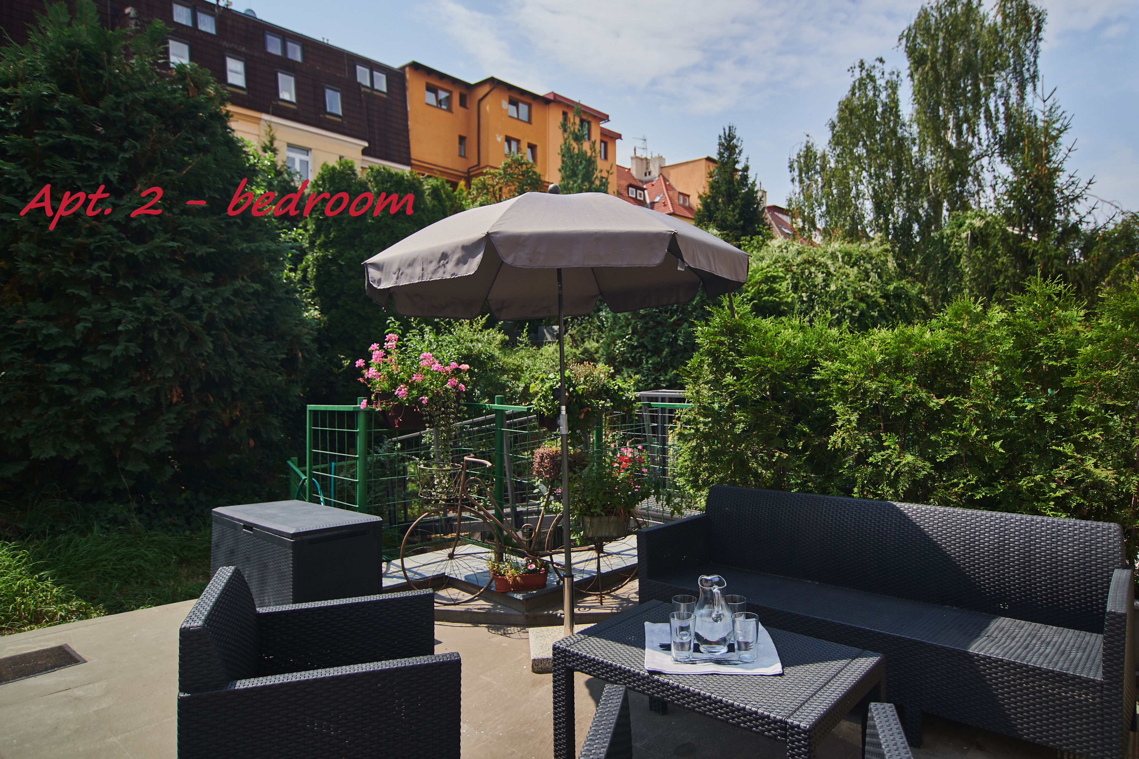 Un espace extérieur aménagé avec des meubles en osier, une table avec des verres et une carafe, et un grand parasol.