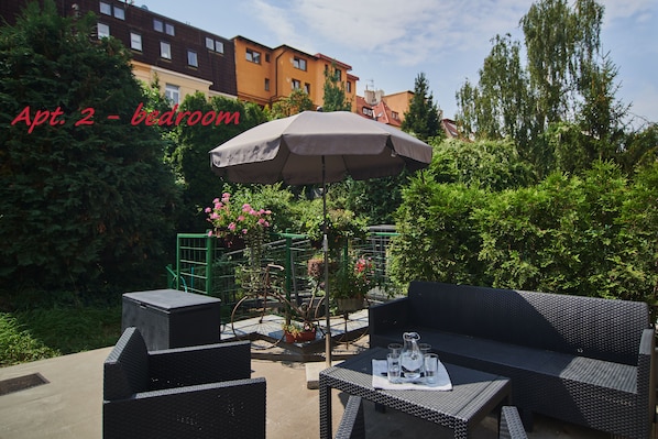 An outdoor seating area with wicker furniture, a table with glasses and a pitcher, and a large umbrella.