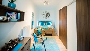 Une chambre à coucher avec un lit en bois, une chaise bleue, une étagère remplie de livres et une horloge murale.