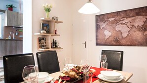 Un coin repas avec une table en bois dressée pour deux personnes, une carte du monde accrochée au mur et une cuisine en arrière-plan.