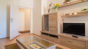 Un salon moderne avec une table basse en verre, un meuble de rangement en bois et un téléviseur à écran plat.