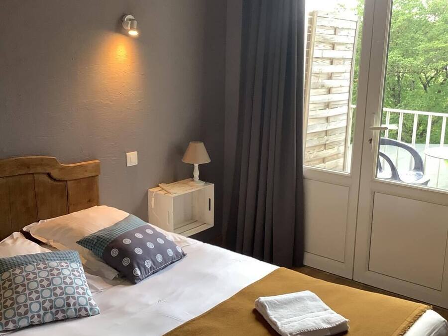 Habitación de hotel con cama, mesita de noche, lámpara, ventana con cortinas y vista a áreas verdes.