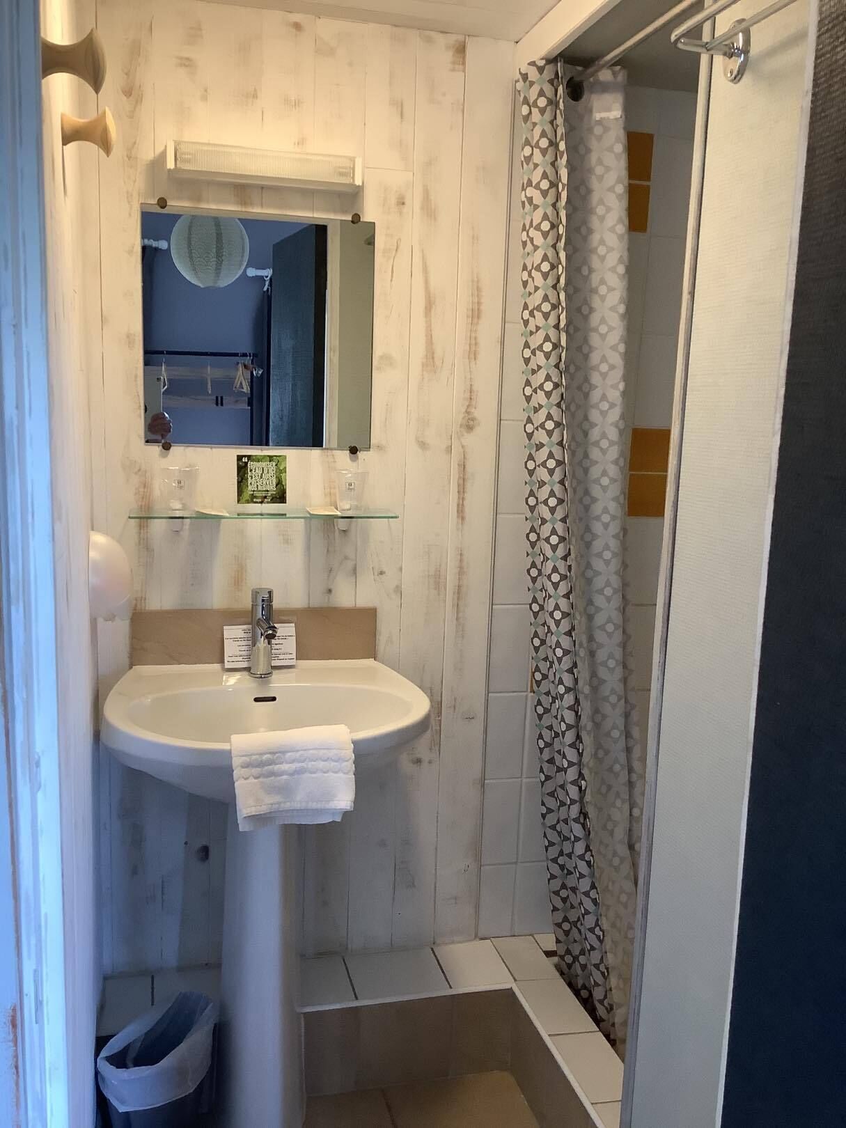 Un baño con lavamanos pedestal, un espejo encima y cortina de ducha.