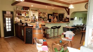 A cozy bar area with wooden beams, a bar counter, and a variety of bottles and glasses. There are two bar stools and a table with a plant. - Logis Hôtel La Borie (Saint-Genies)