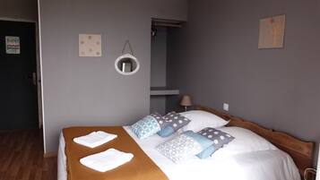 A neatly made bed with a brown blanket and patterned pillows, a round mirror on the wall, and a door to the left.