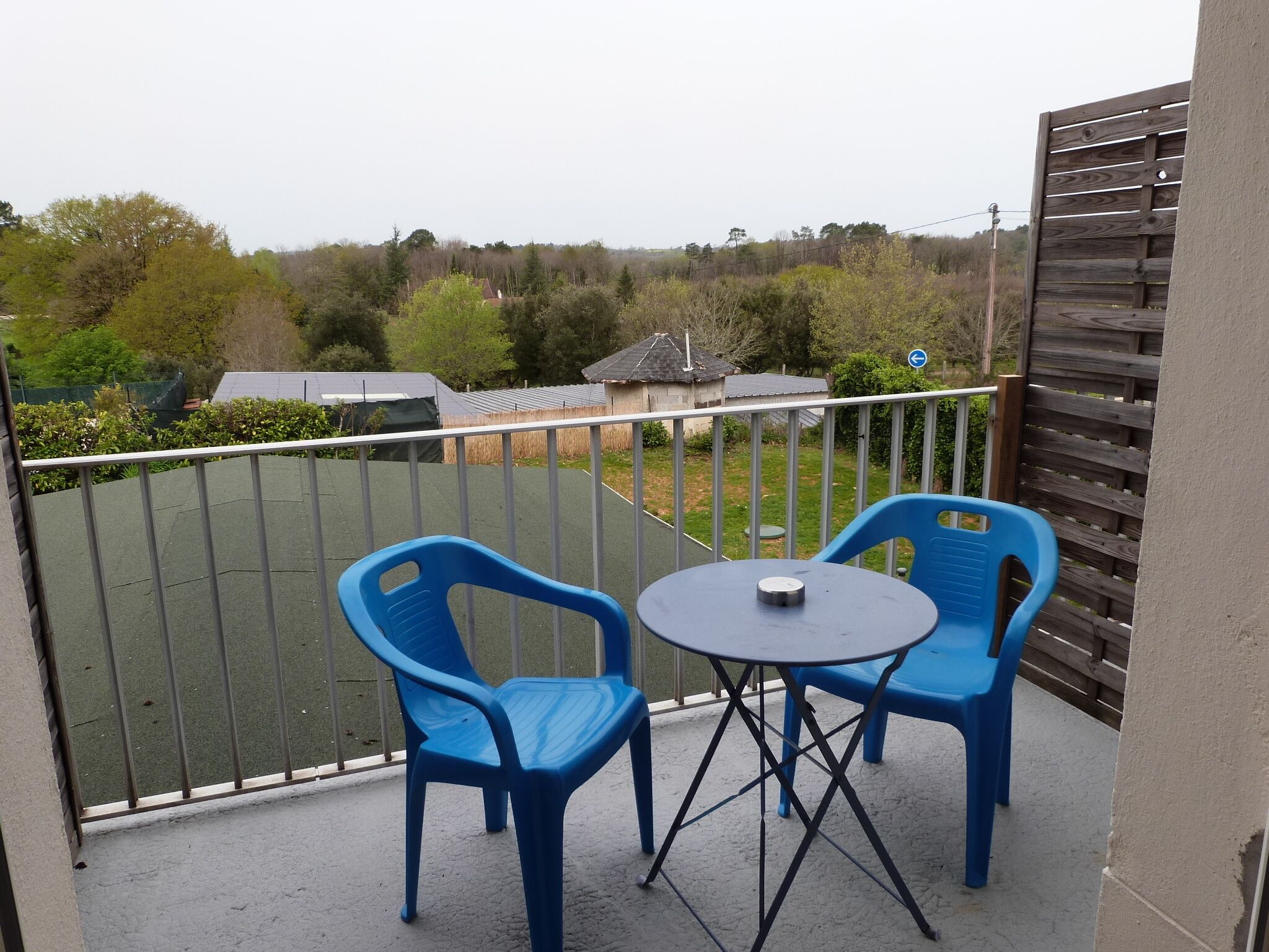A balcony with two blue plastic chairs and a small round table.