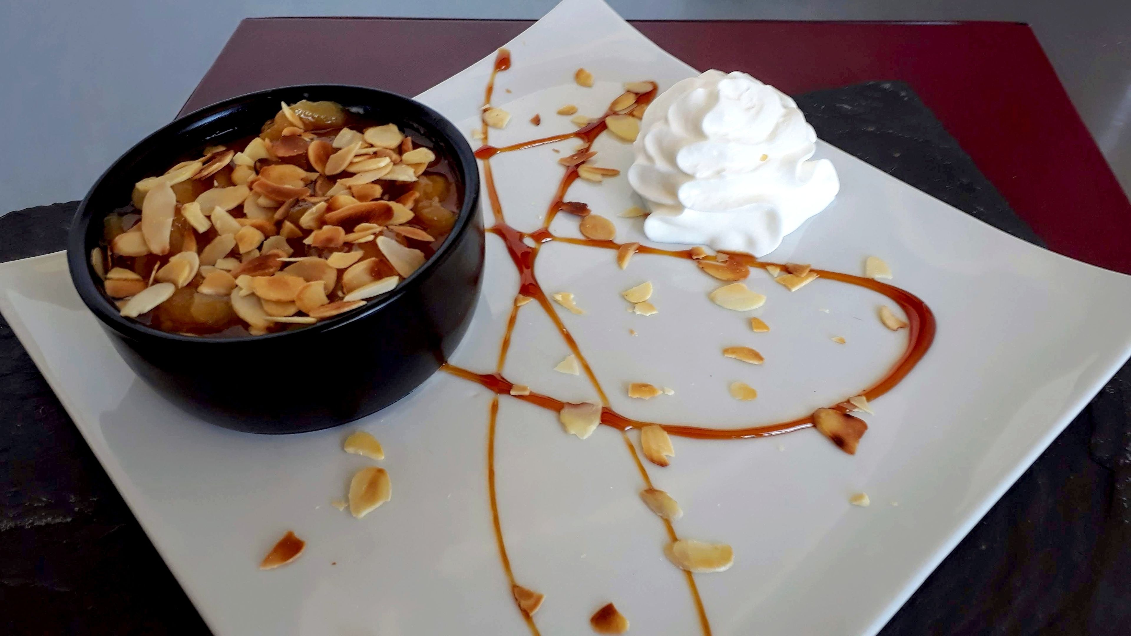 A dessert plate with a bowl of caramel and almonds, and a scoop of ice cream with whipped cream and drizzled caramel.