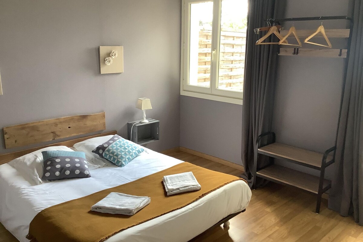 A bedroom with a bed, a bedside table with a lamp, a window with curtains, and a wooden bench.