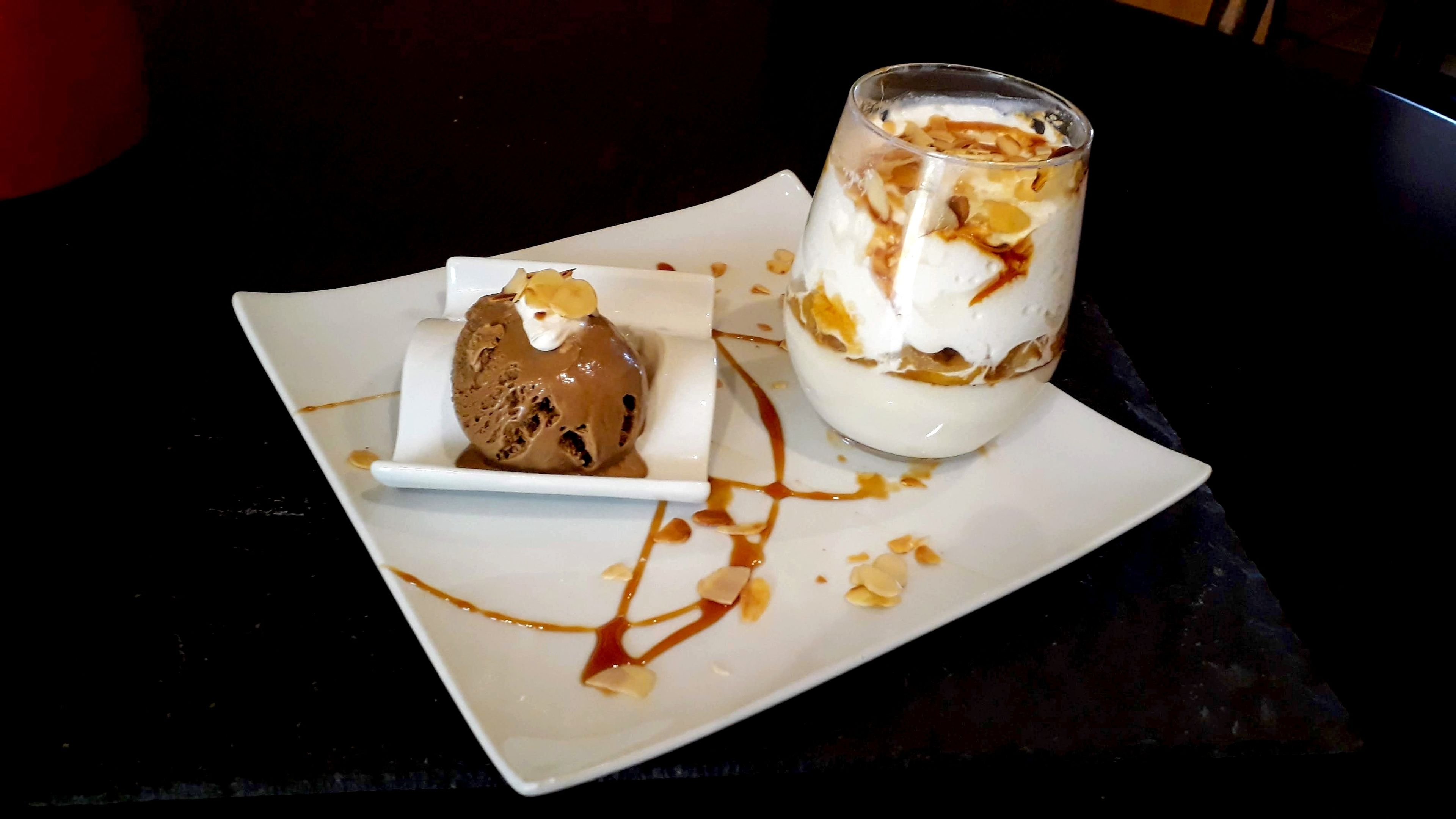 Um prato de sobremesa com uma bola de sorvete de chocolate e um copo de sobremesa em camadas com chantilly e nozes.