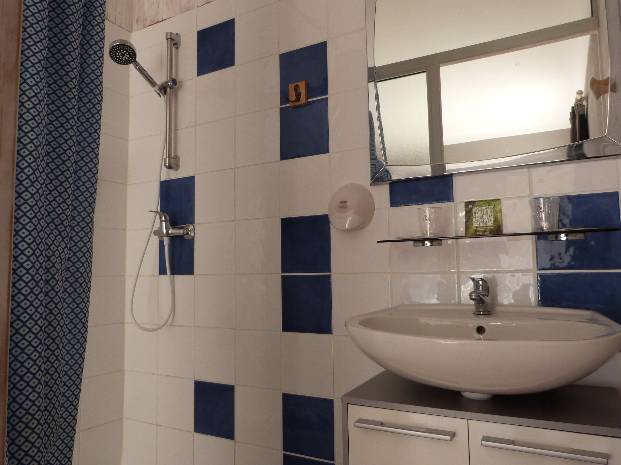 Un baño con lavamanos blanco, un espejo y una ducha con cabezal de ducha manual.