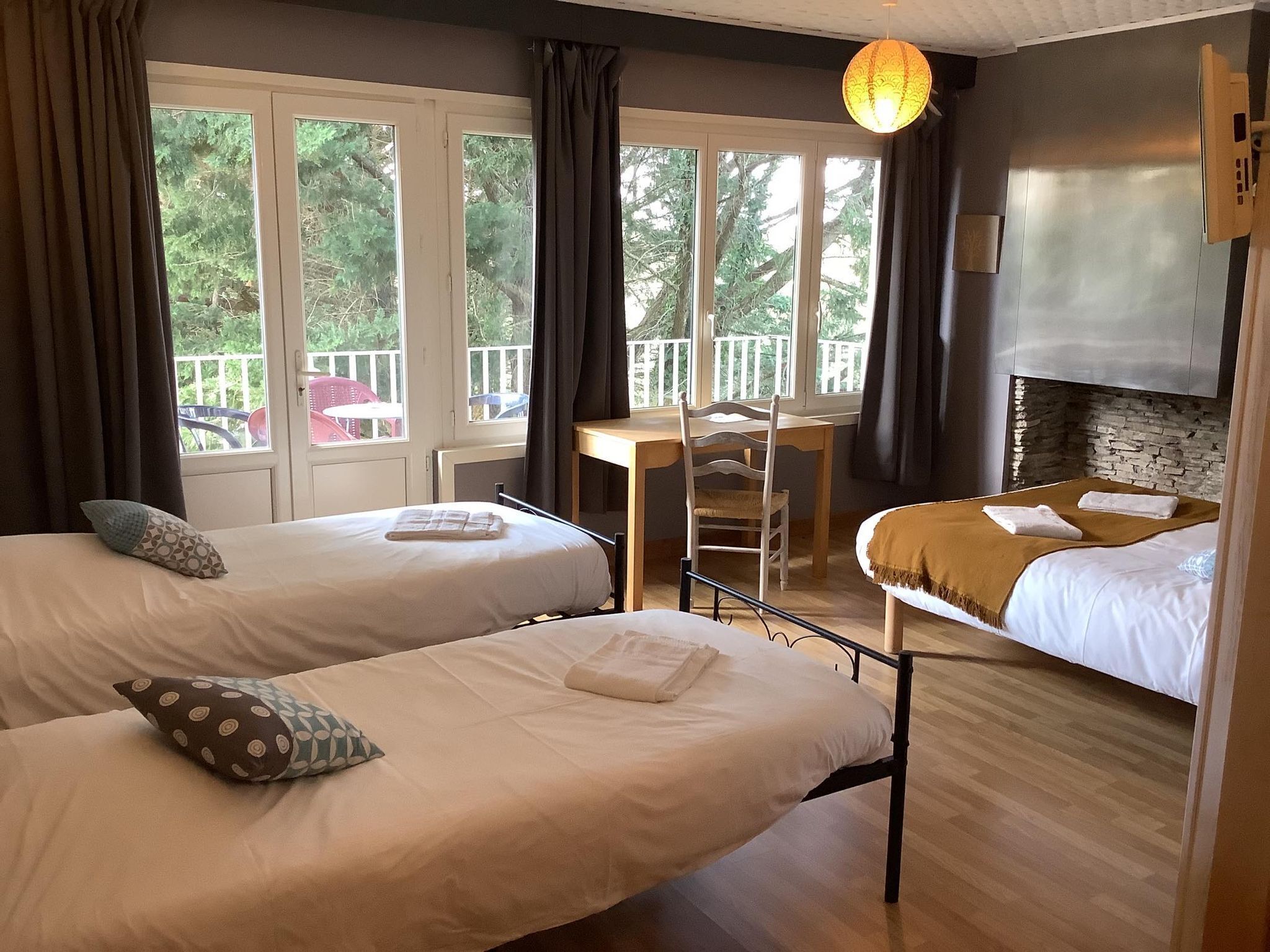 A room with two beds, a wooden desk, a chair, a balcony with a railing, and a stone wall.