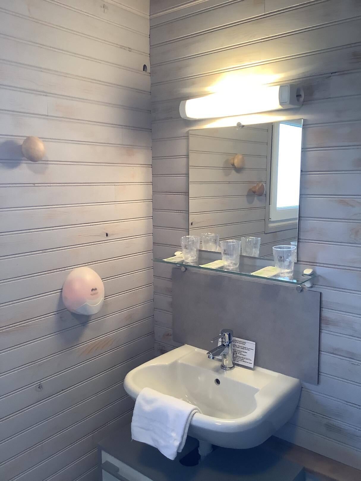 A bathroom with a white sink, a mirror, and a soap dispenser on the wall.