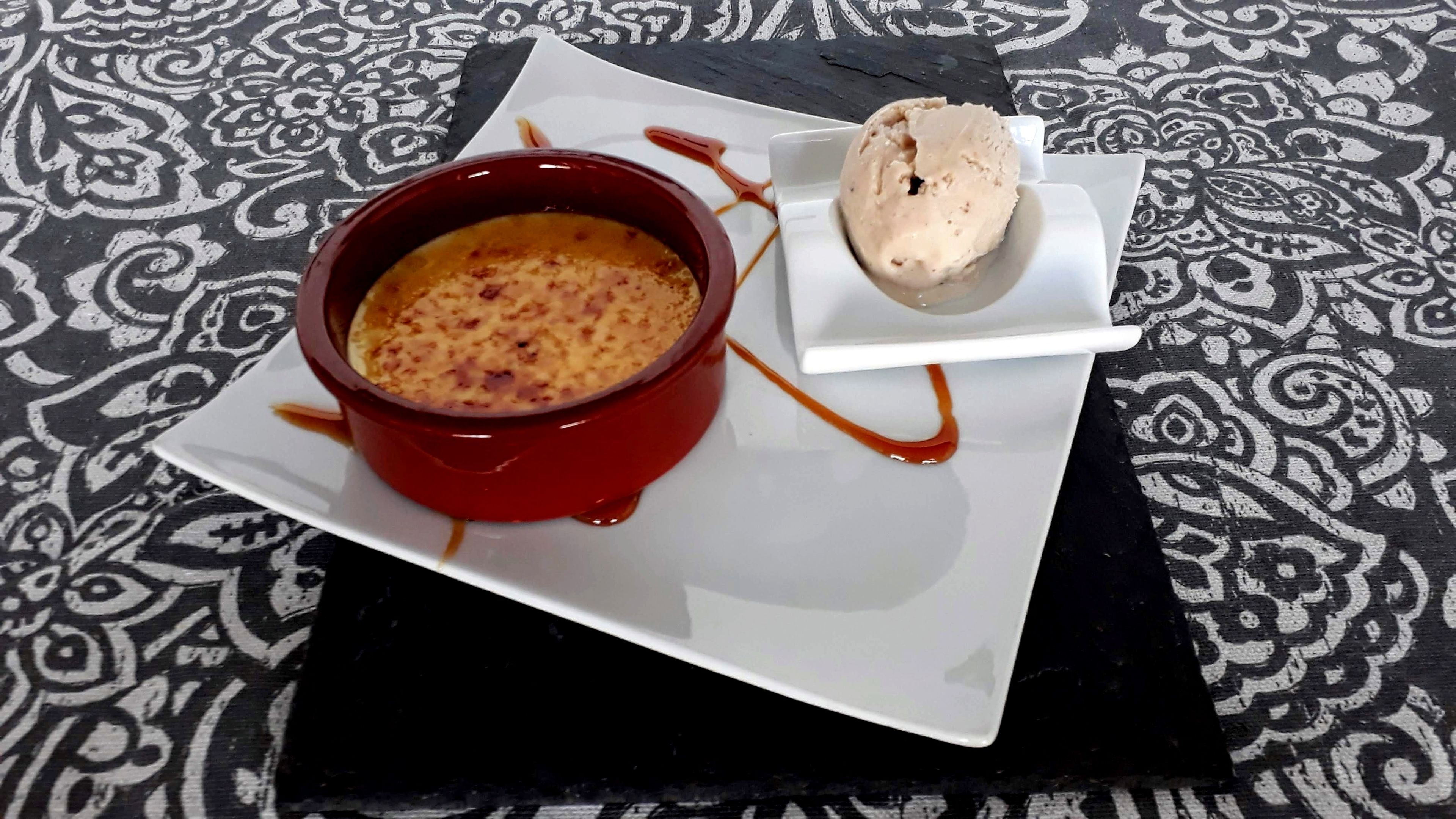 Un dessert composé d’une préparation rouge cuite au four et d’une boule de glace, le tout présenté sur une assiette blanche, posée sur une nappe à motifs.