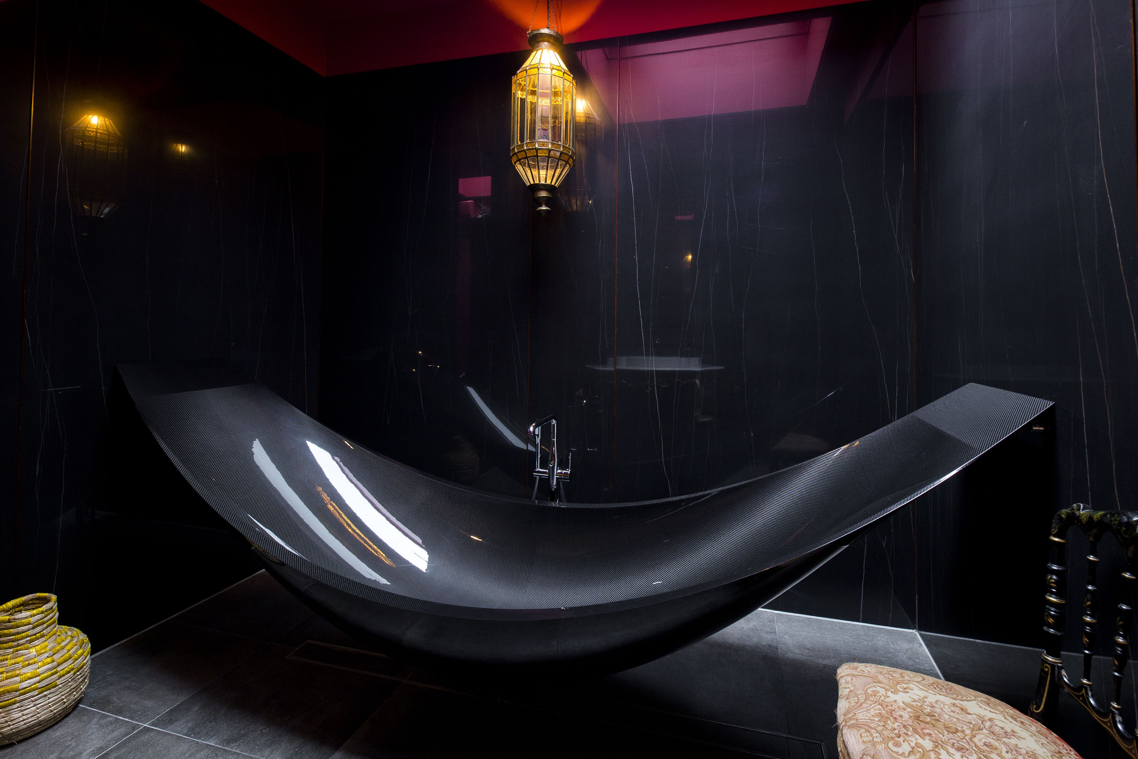 Un baño moderno con una bañera curvada, una lámpara colgante y una silla de madera.
