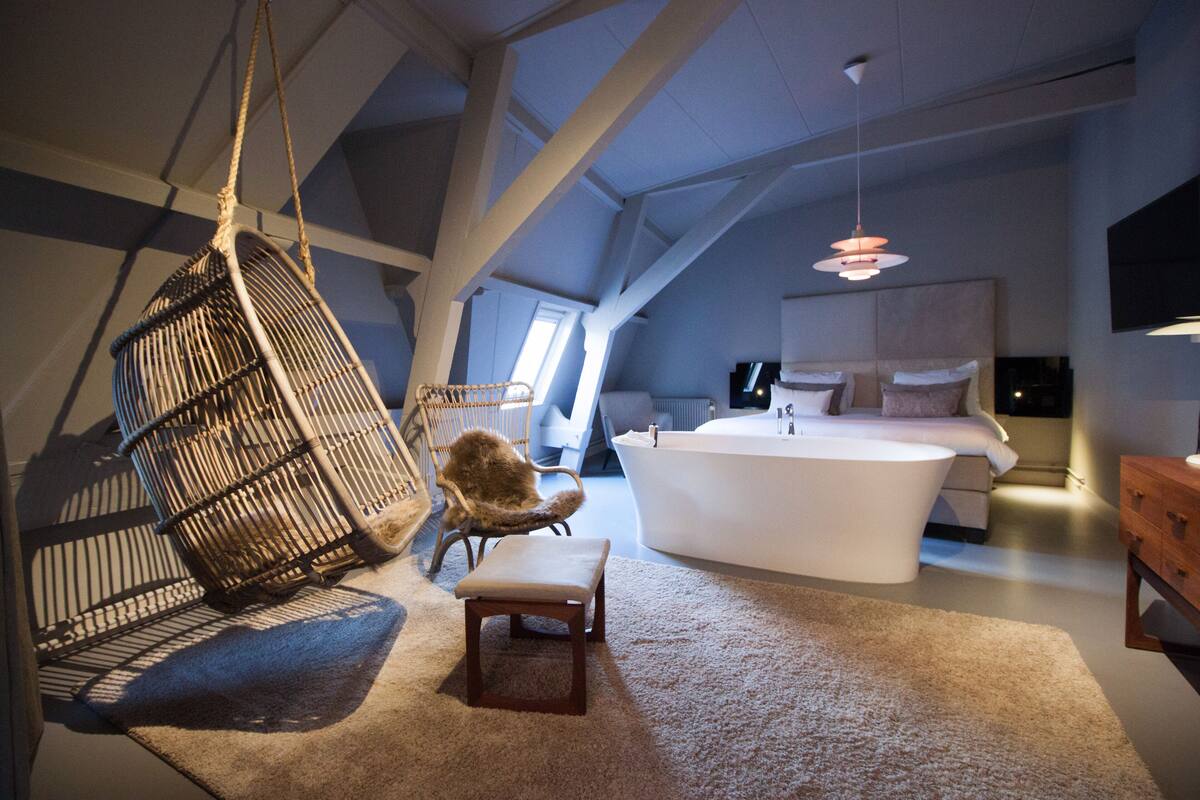 A modern bedroom with a large bed, a hanging chair, and a bathtub.