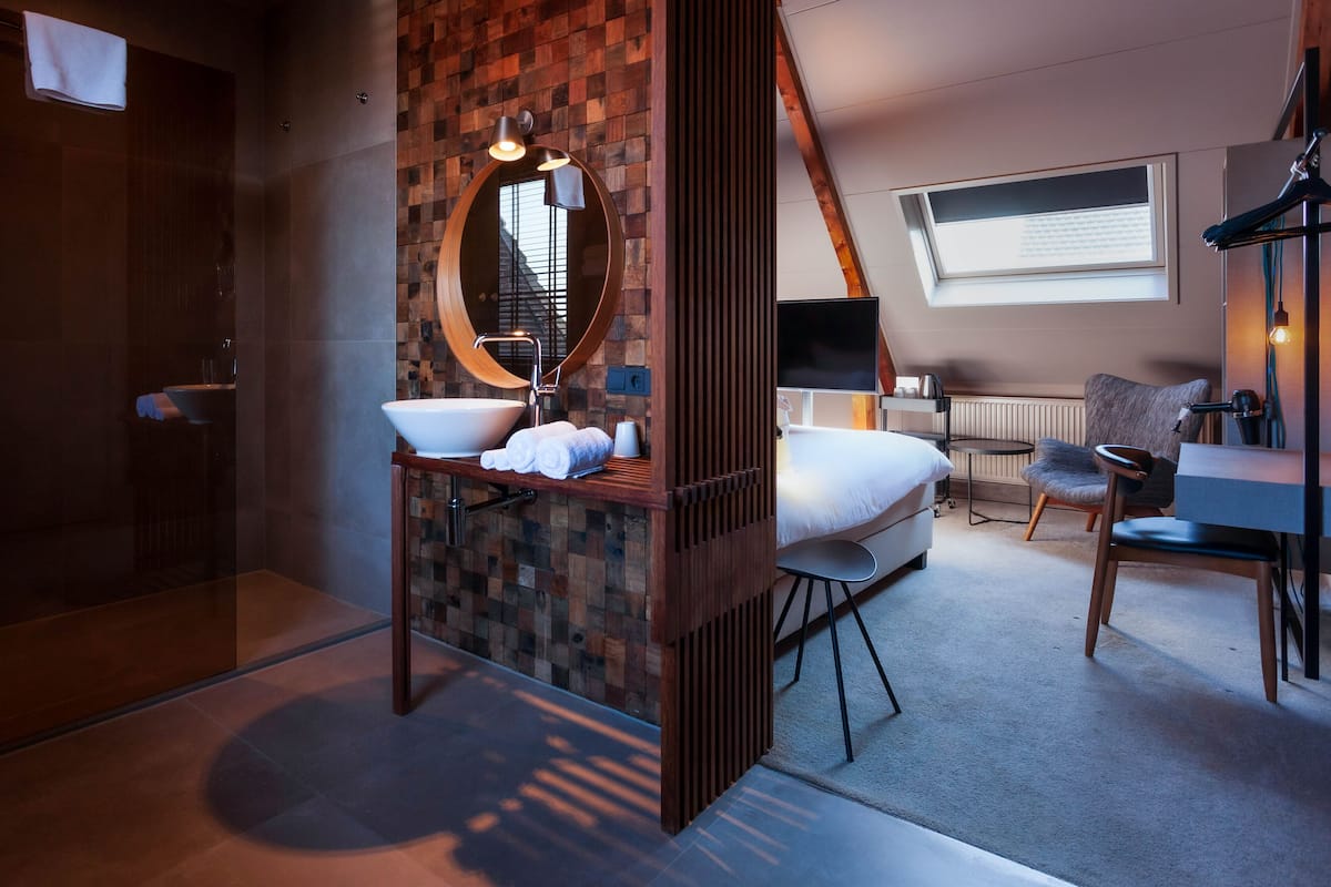 A modern hotel room with a wooden accent wall, a round mirror, a large bed, a desk, and a chair.