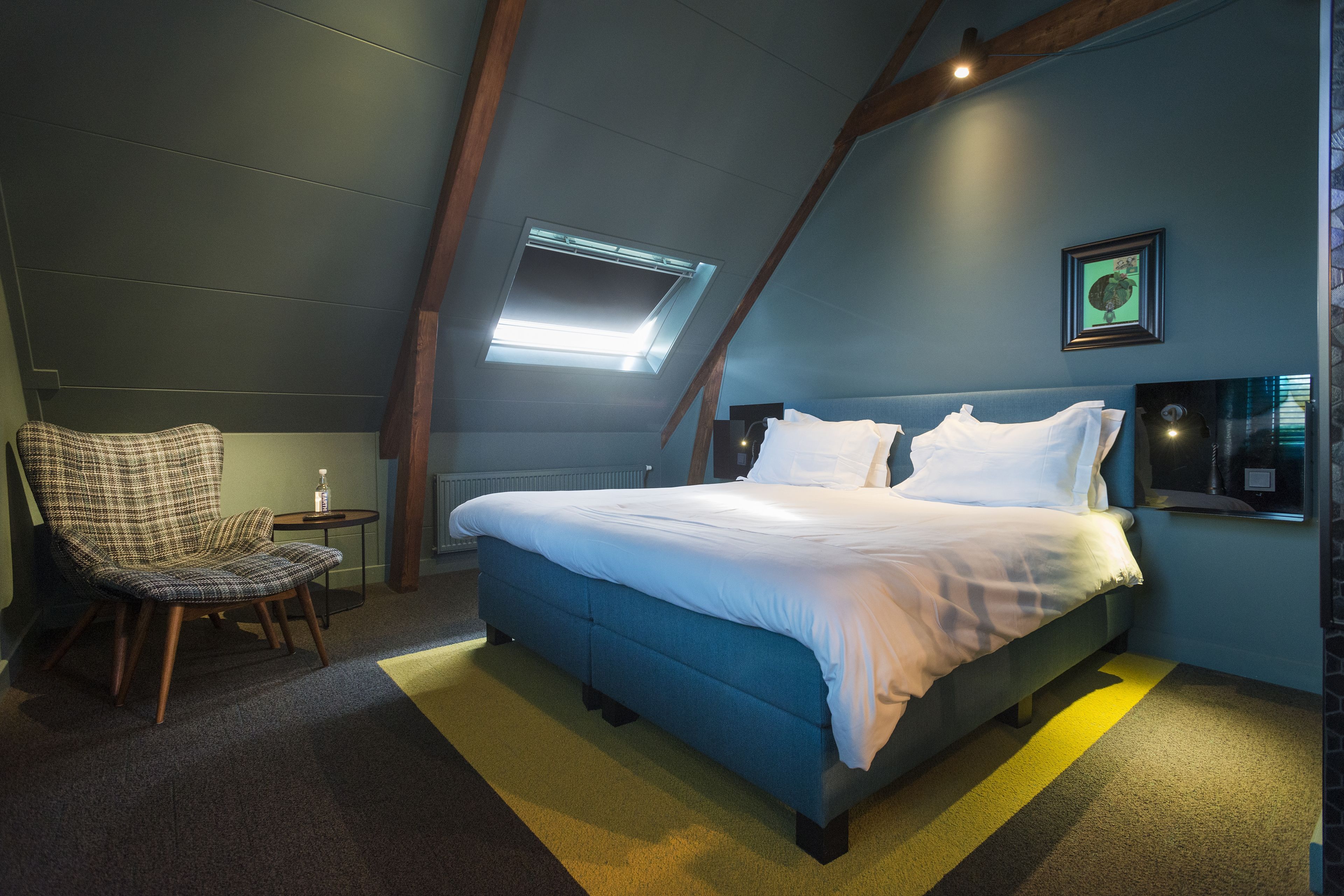 Un dormitorio con cama, una silla, una mesita y un tragaluz.
