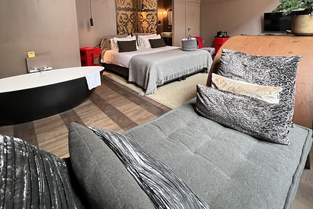 A modern hotel room with a large bed, a sofa, and a desk area.