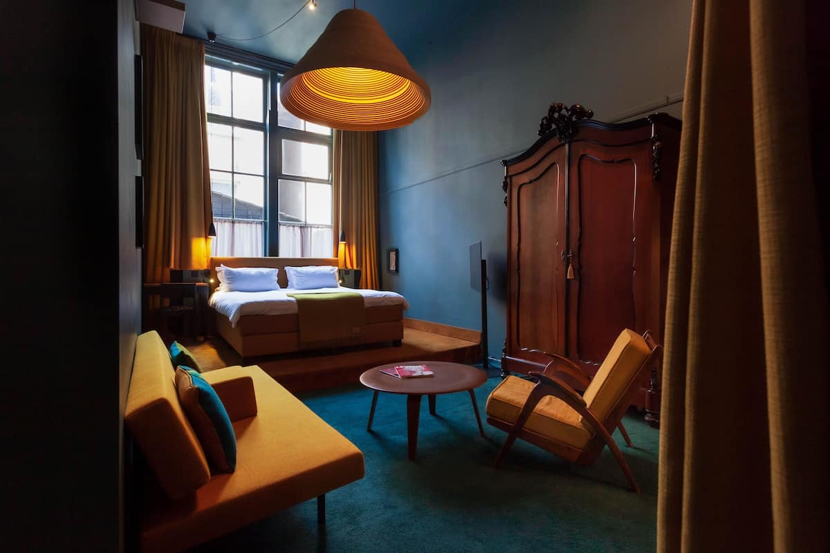A hotel room with a bed, sofa, armchair, round table, and wardrobe.