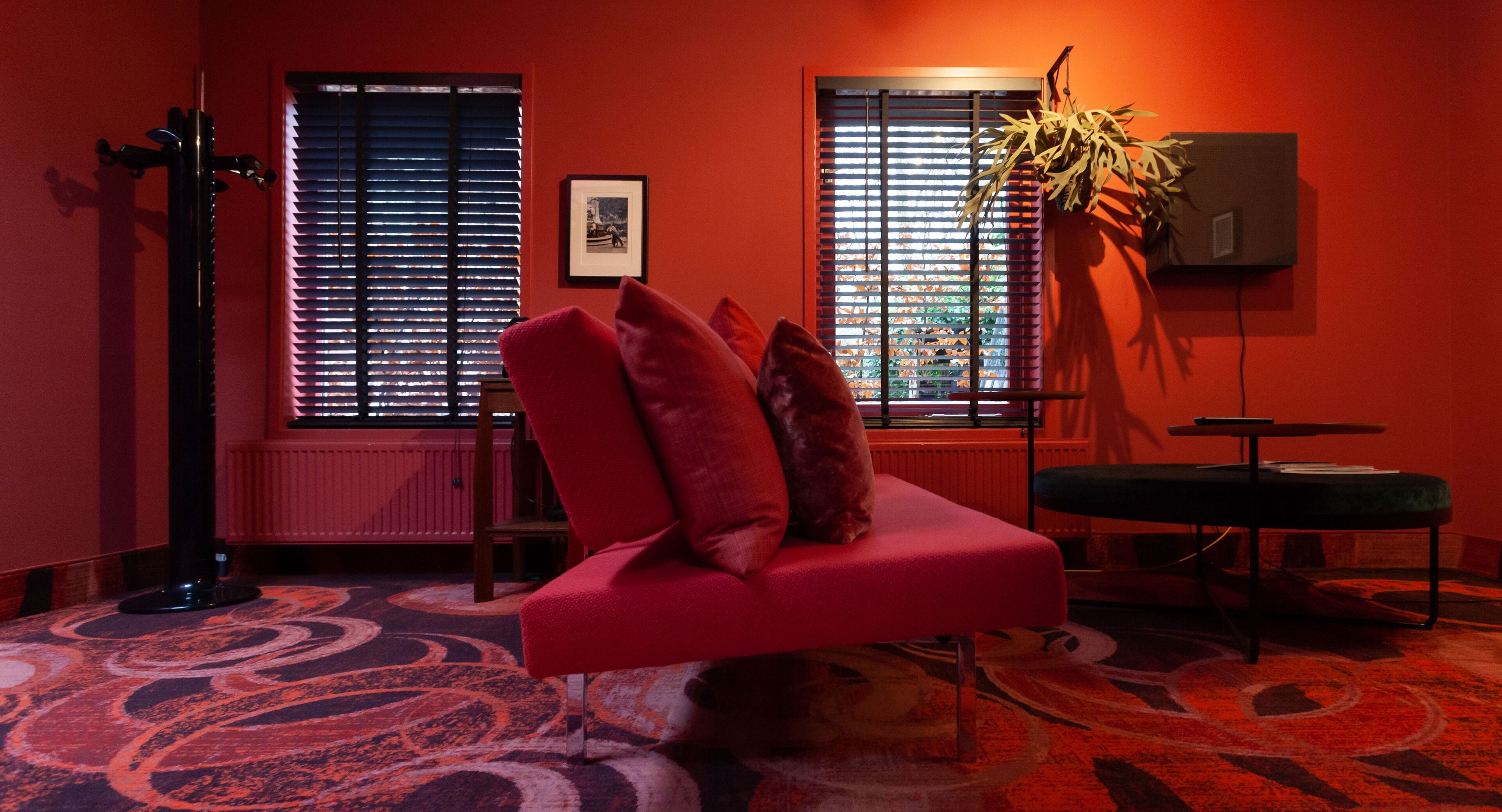 A modern living room with a red sofa, a green ottoman, and a patterned carpet.