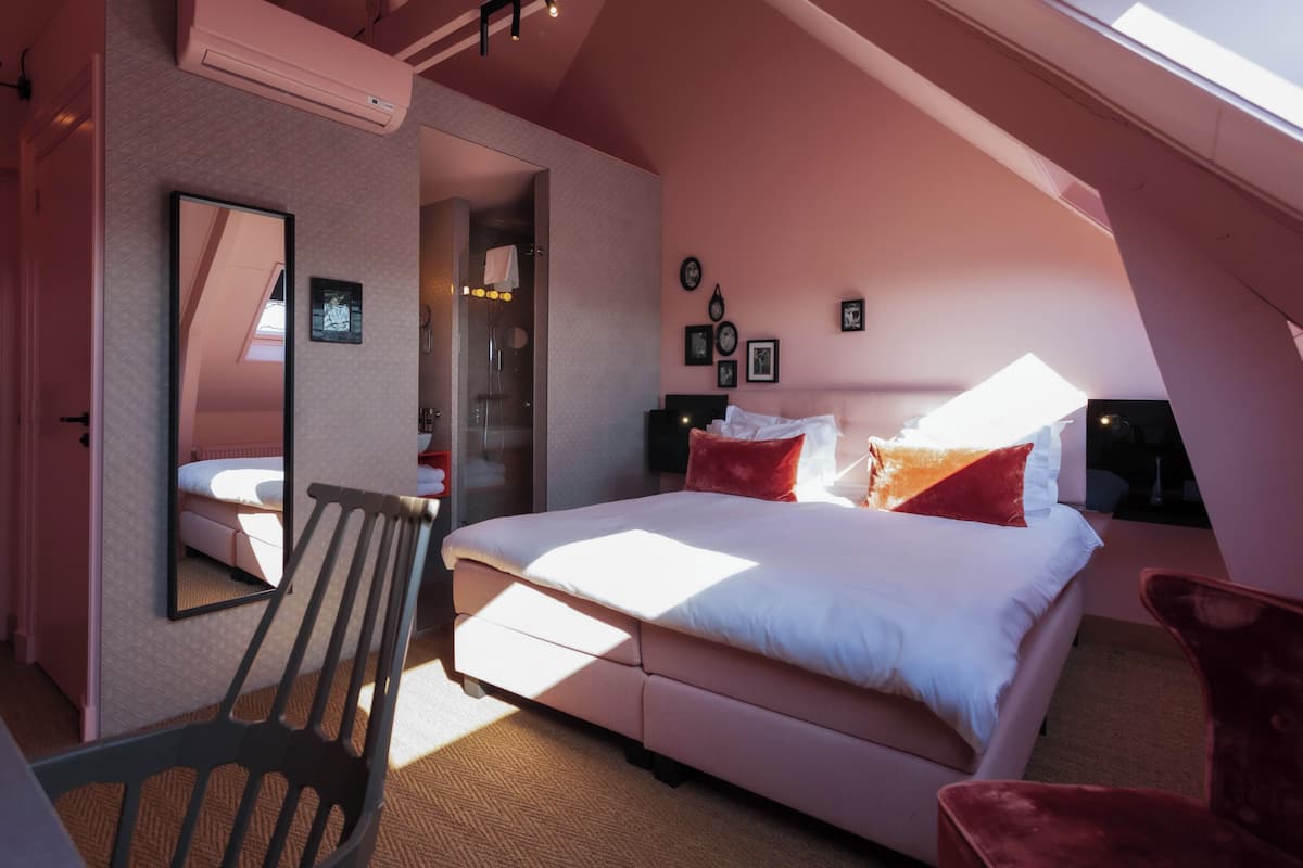 A bedroom with a large bed, a chair, a mirror, and a wardrobe.