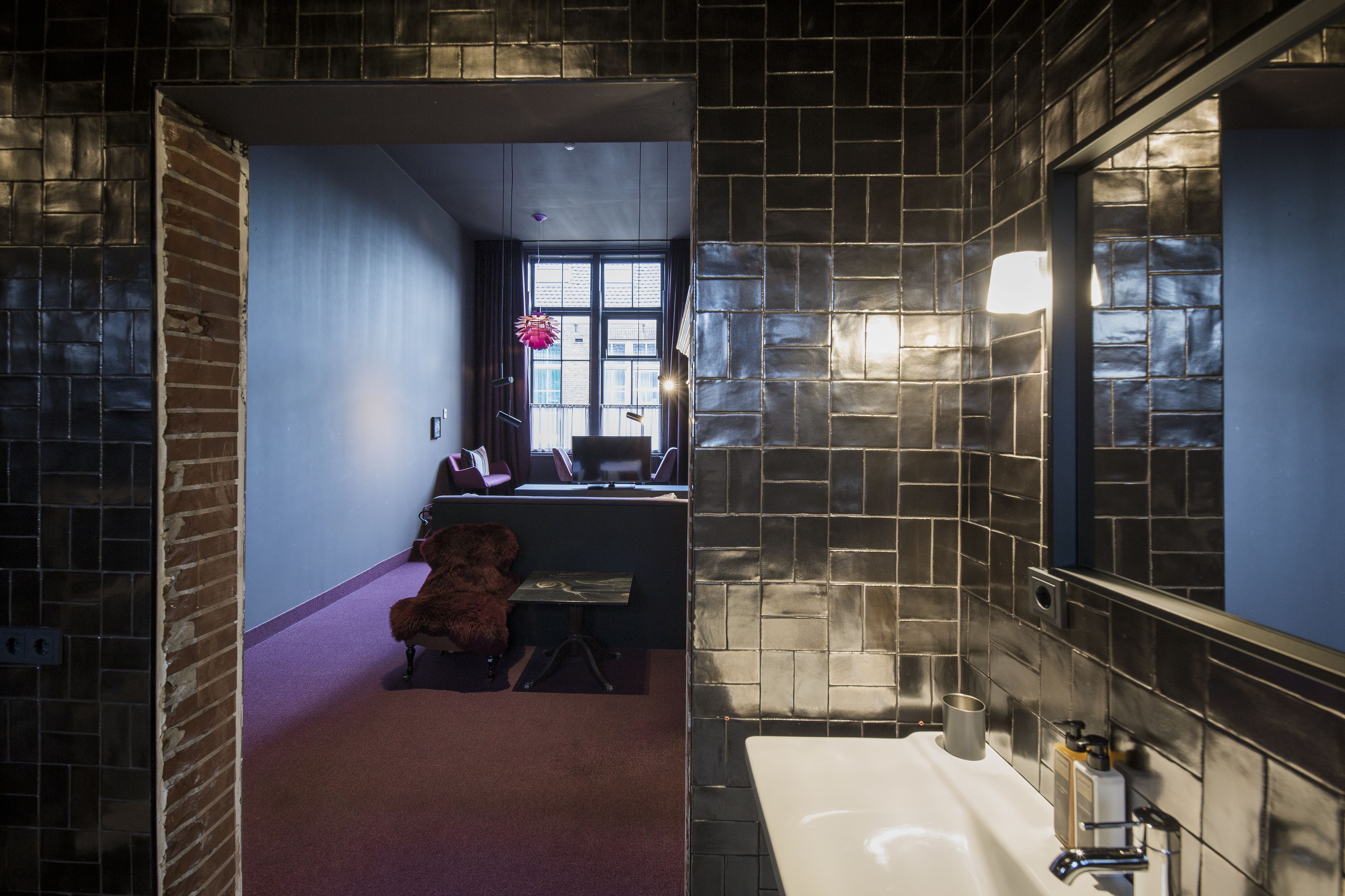 A modern bathroom with a large mirror, a white sink, and a small table with a teddy bear.