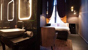 Quarto de hotel moderno com um espelho grande, pia, cama e uma cadeira.