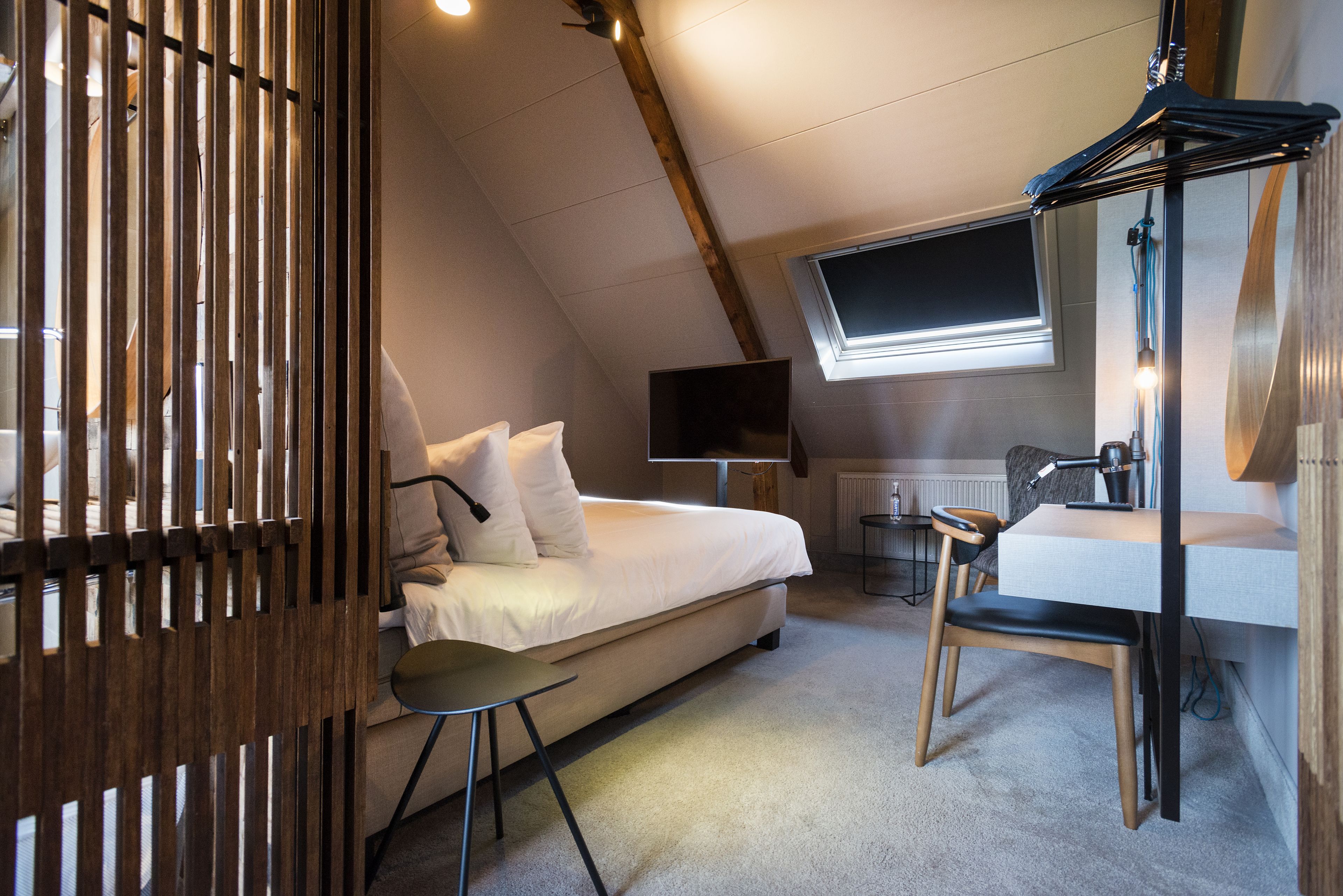 A bedroom with a bed, a desk, a chair, a TV, and a window.