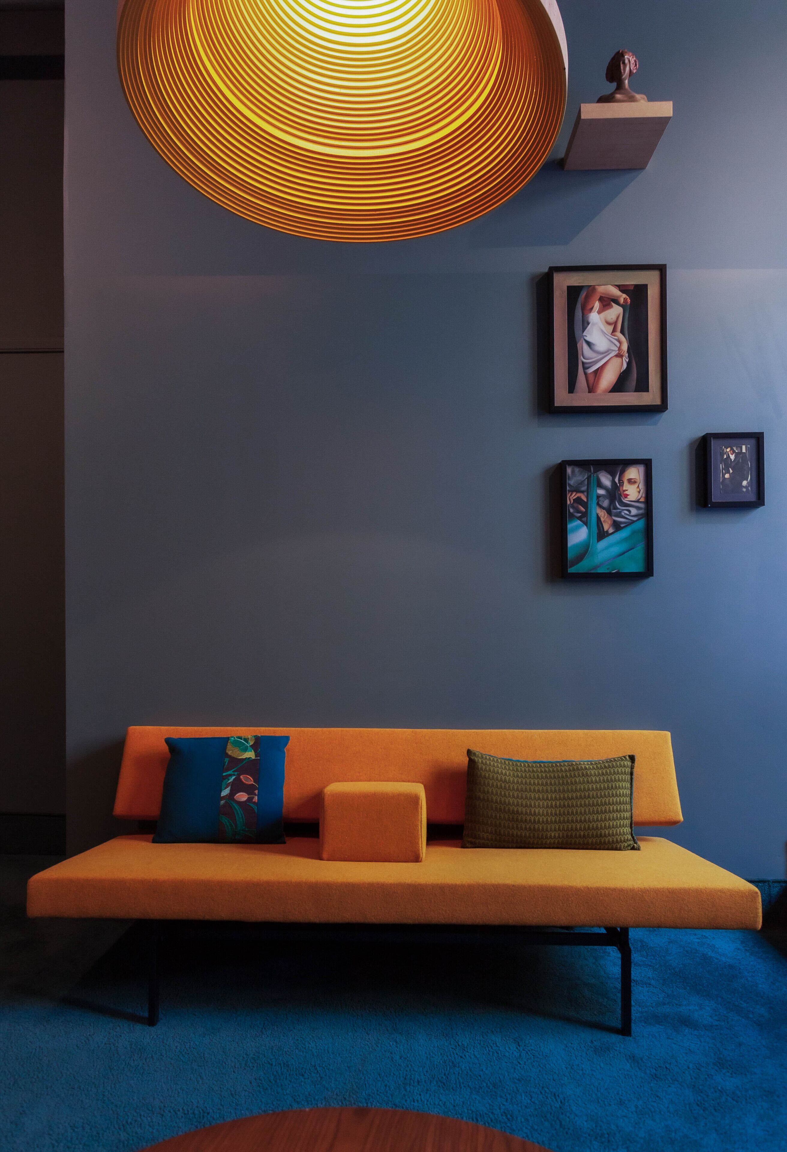 Un salon moderne avec un canapé, un grand luminaire suspendu et des œuvres d’art encadrées accrochées au mur.