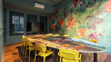 A conference room with a large oval table, yellow chairs, and a floral mural on the wall.