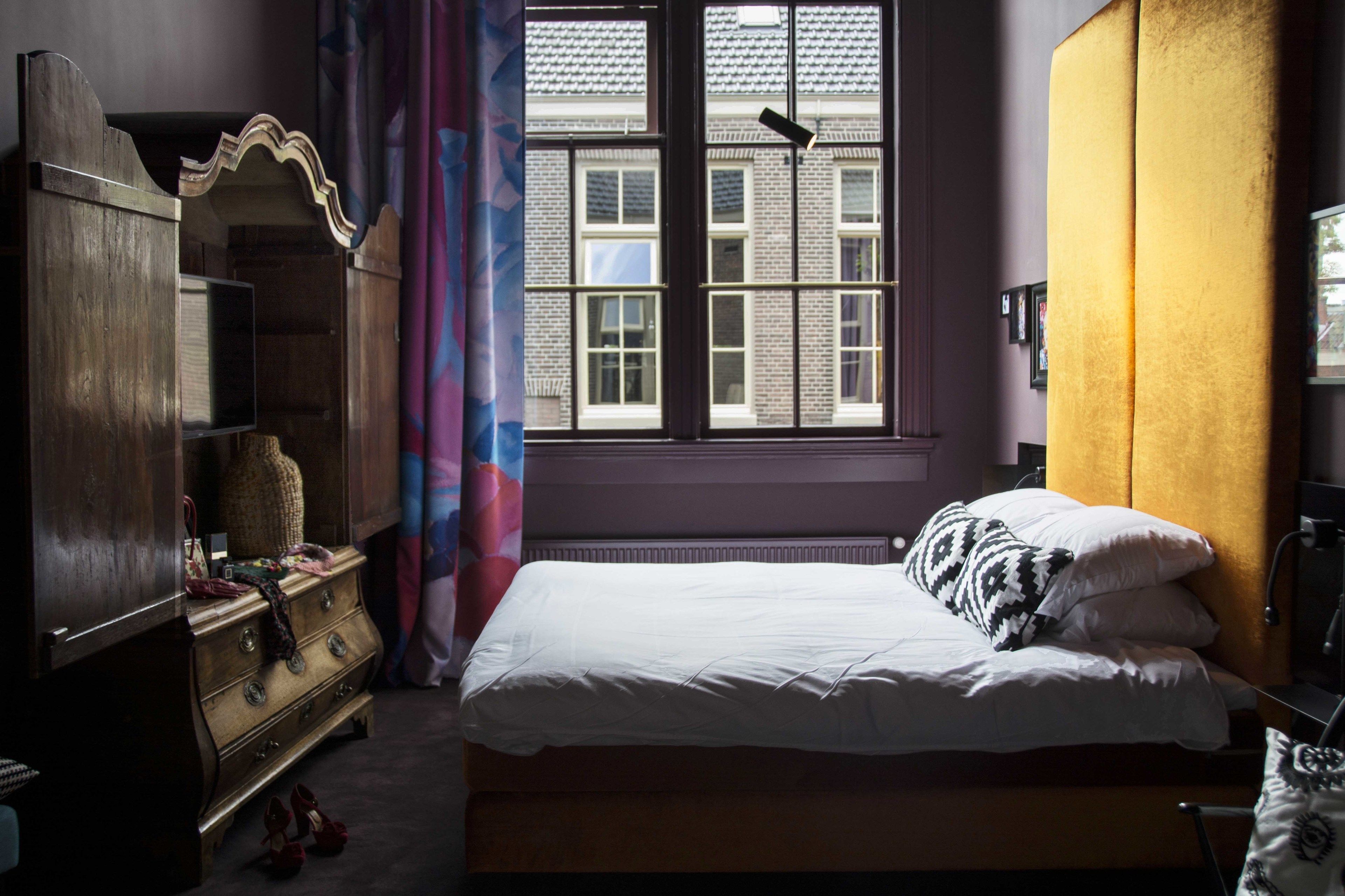 Ein Schlafzimmer mit Bett, Kommode und einem Fenster mit Vorhängen.