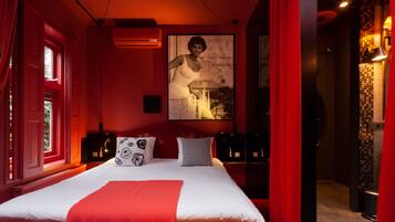 A hotel room with a large bed, red curtains, a mounted picture, and a red wall.