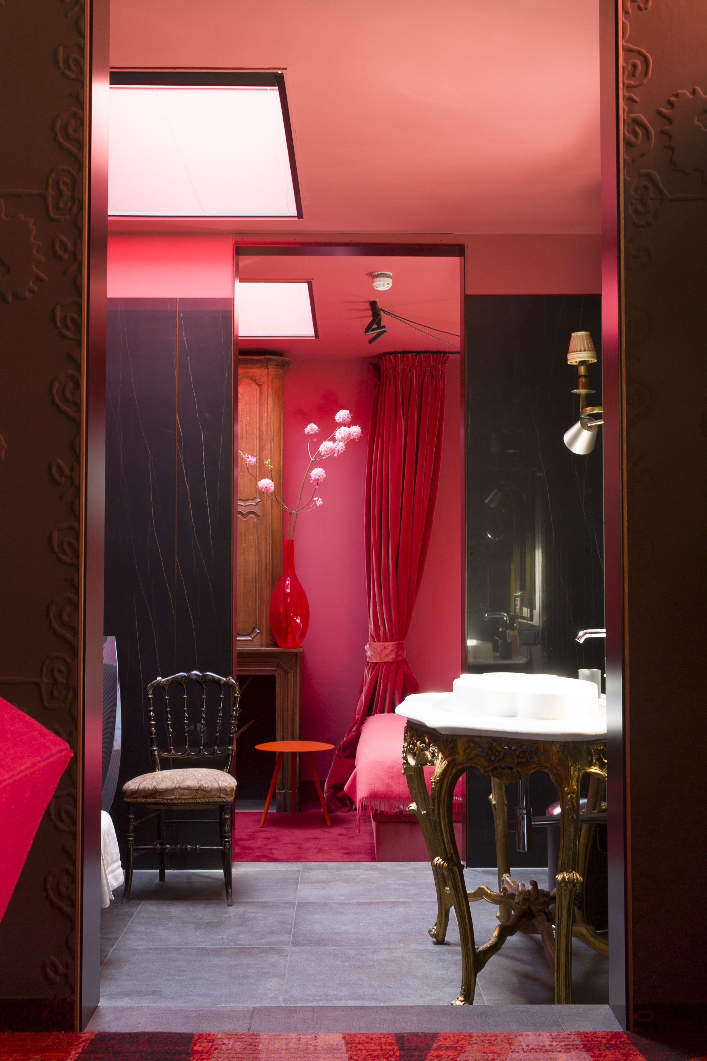 A room with a red and black color scheme, a wooden chair, a small round table, and a large mirror.