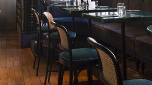 A restaurant interior with wooden floors, dark walls, and a large window. There are tables and chairs, and a vase with a plant on the wall. - Boutiquehotel Staats (Haarlem)