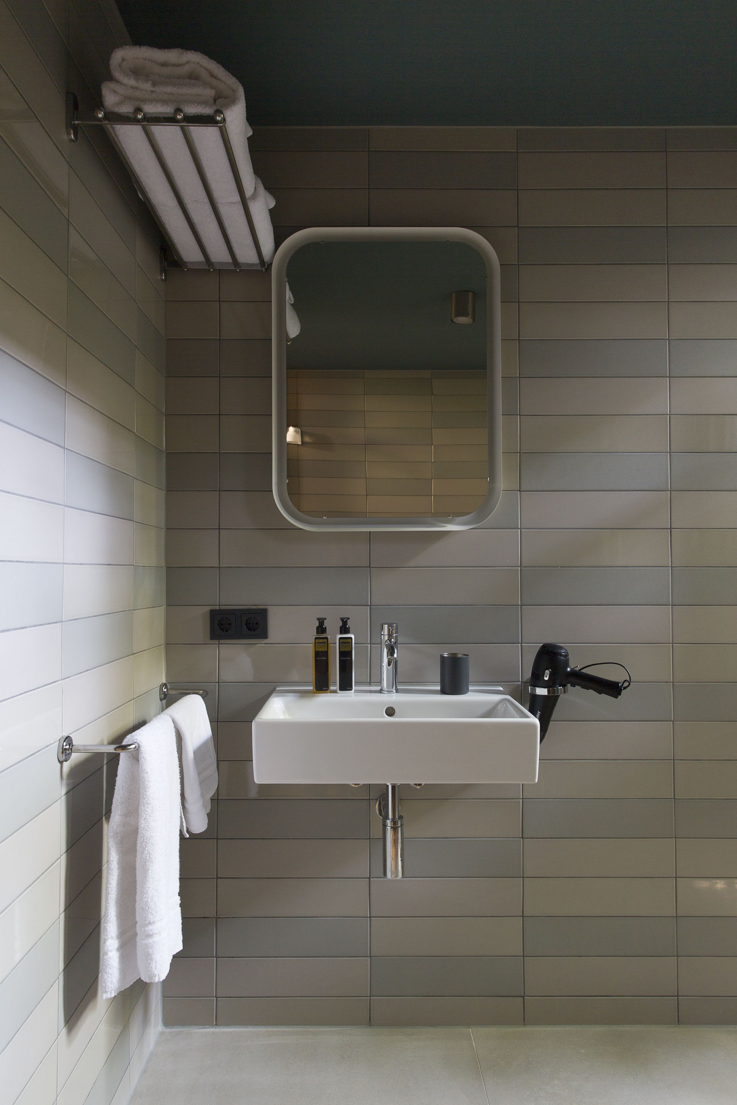 Un baño moderno con un lavamanos blanco, un espejo y un perchero para toallas.