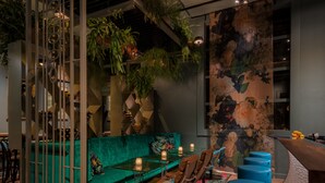 A modern interior with a teal sofa, wooden flooring, and a bar area with stools. - Boutiquehotel Staats (Haarlem)