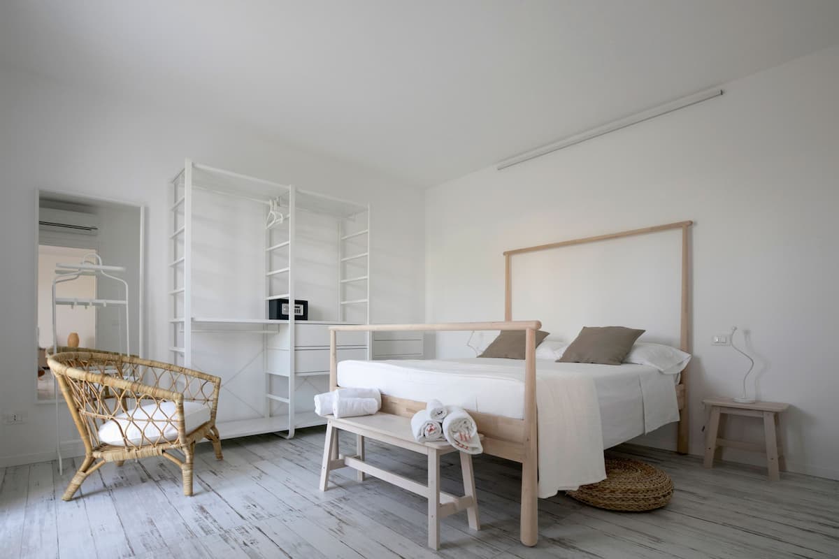 A minimalist bedroom with a bed, a wicker chair, and a built-in wardrobe.