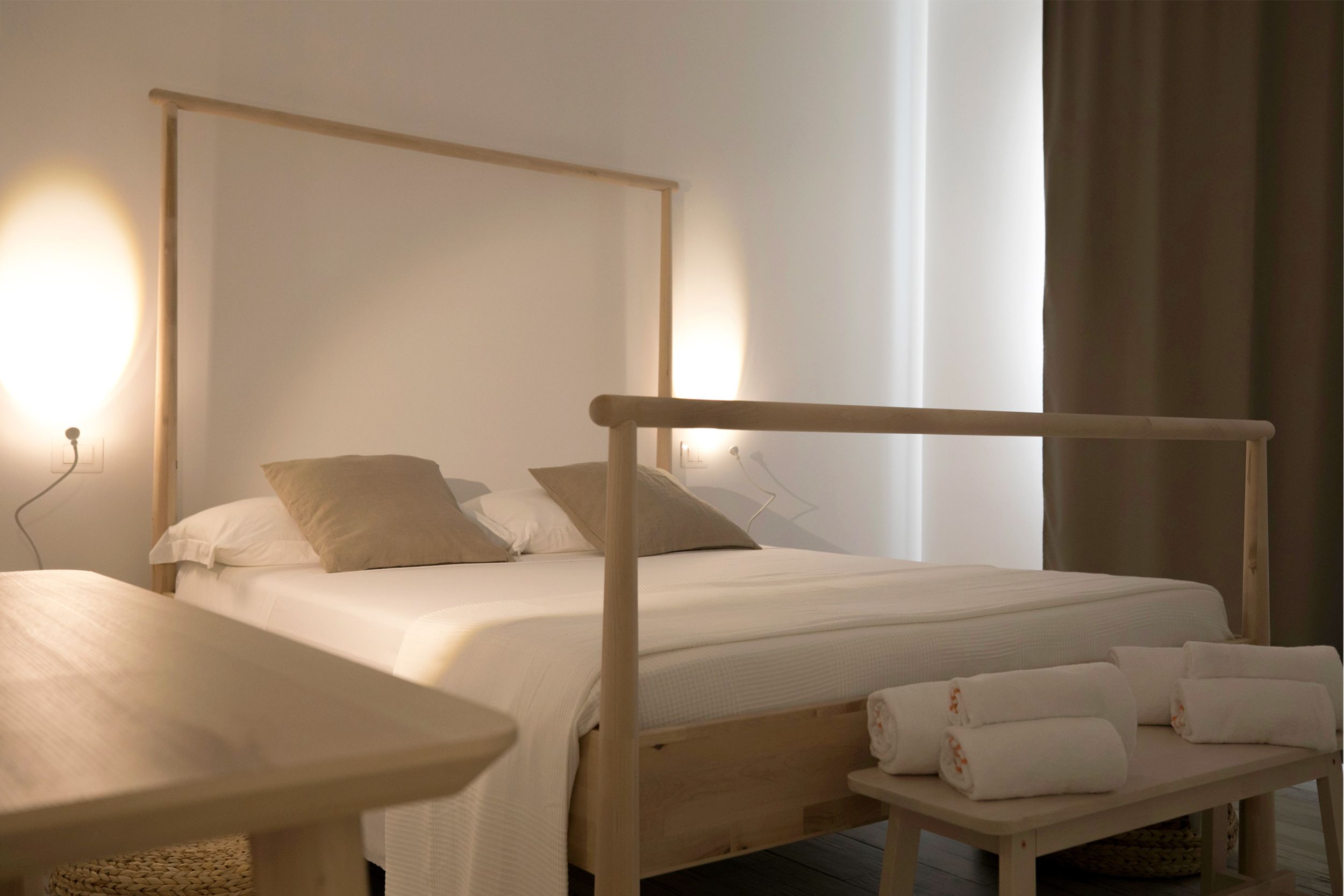 Un dormitorio ordenado con estructura de cama de madera, una mesita de noche y un pequeño banco con toallas.