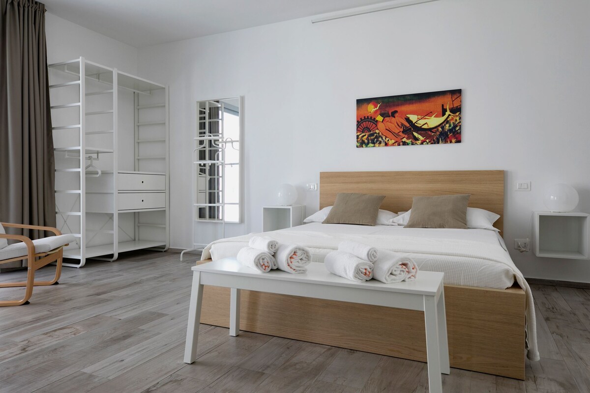 Une chambre à coucher avec un lit, une table de chevet, une chaise, une armoire et un tableau accroché au mur.