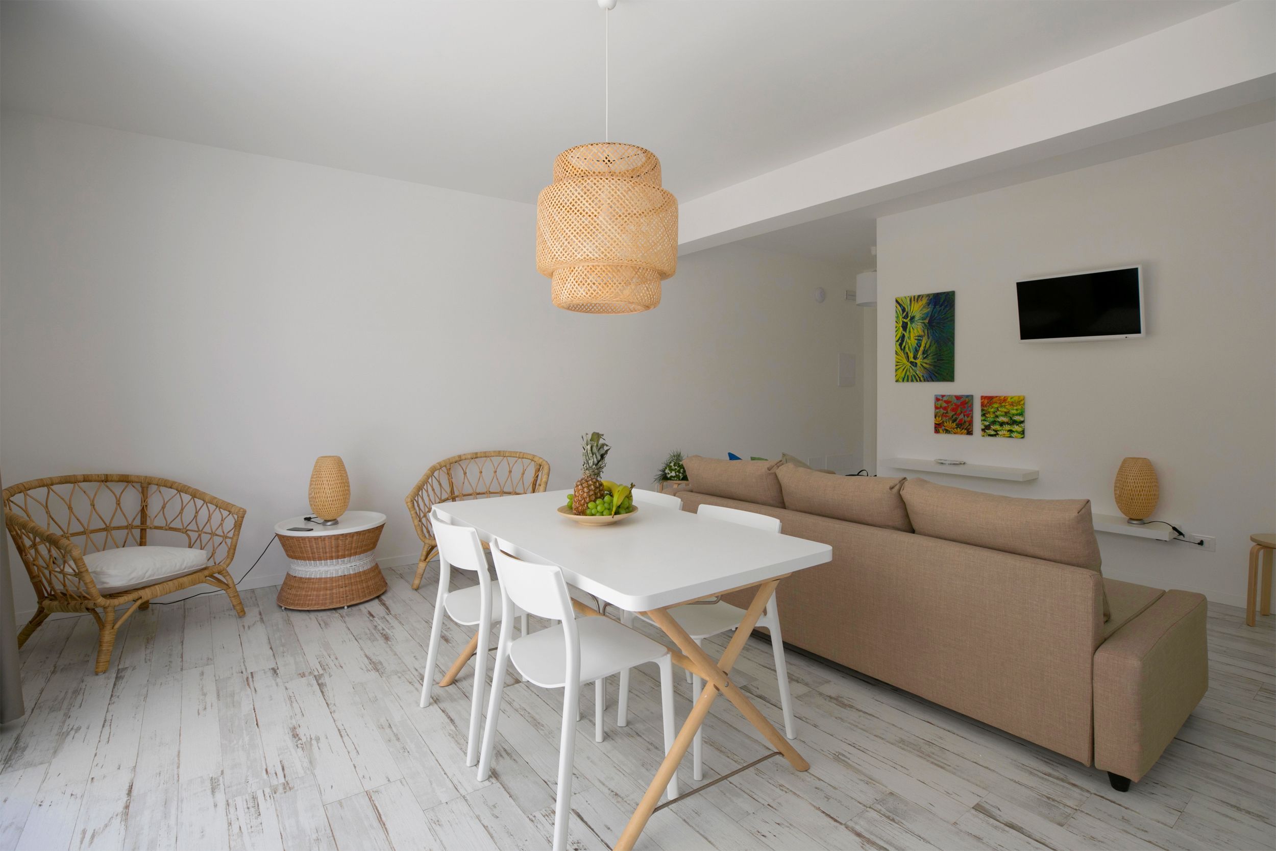 A modern living space with a white dining table, wicker chairs, a beige sofa, and a hanging light fixture.