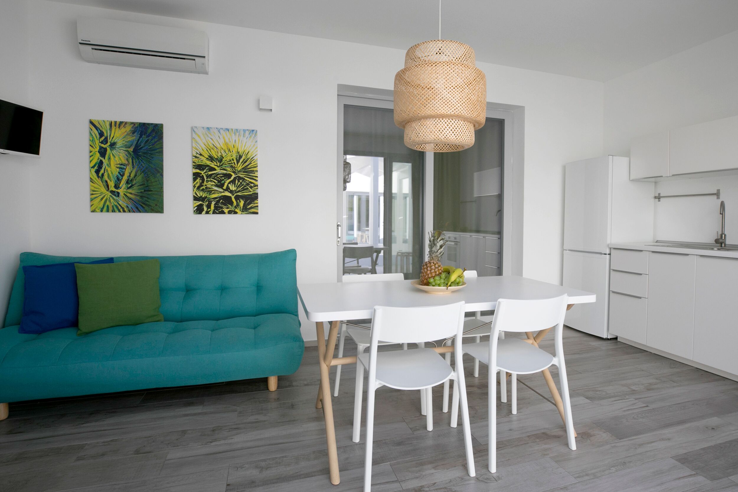 A modern kitchen with white cabinets, a white dining table with chairs, and a teal sofa with cushions.