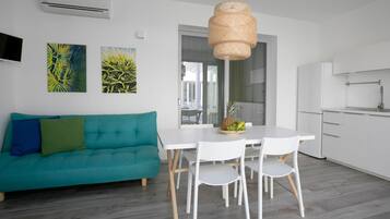 Una cucina moderna con mobili bianchi, un tavolo da pranzo bianco con sedie e un divano color petrolio con cuscini.