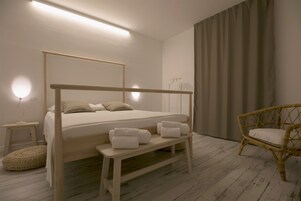 Un dormitorio con una cama de madera con dosel, una mesita de noche con toallas, una silla de mimbre y una lámpara de noche.