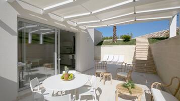Une terrasse extérieure couverte, aménagée avec une table à manger, des chaises et une petite table sur laquelle est posée une plante.