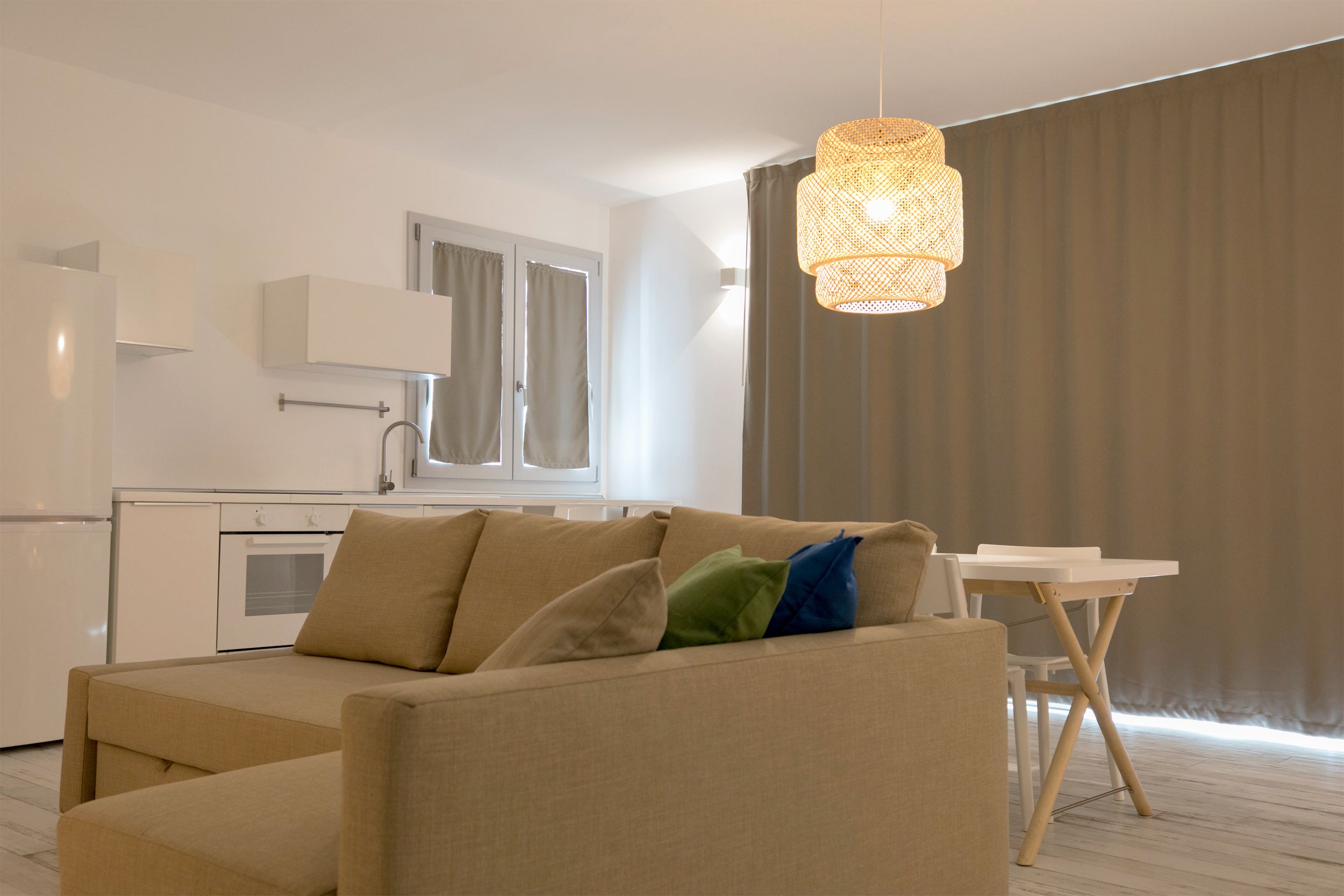 Ein modernes Wohnzimmer mit einem beigen Sofa, einem kleinen weißen Tisch und einer Pendelleuchte.