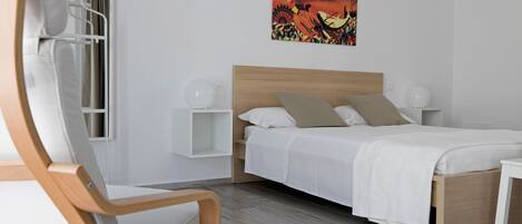 A modern bedroom with a wooden bed frame, white bedding, a wall-mounted artwork, and a bedside table with a lamp.