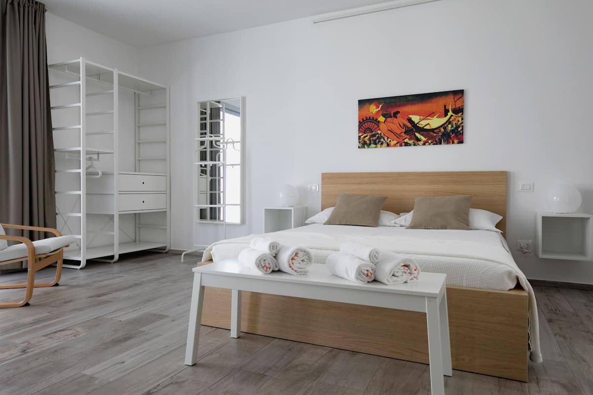 A modern bedroom with a wooden bed, white bedside tables, a built-in wardrobe, and a painting on the wall.