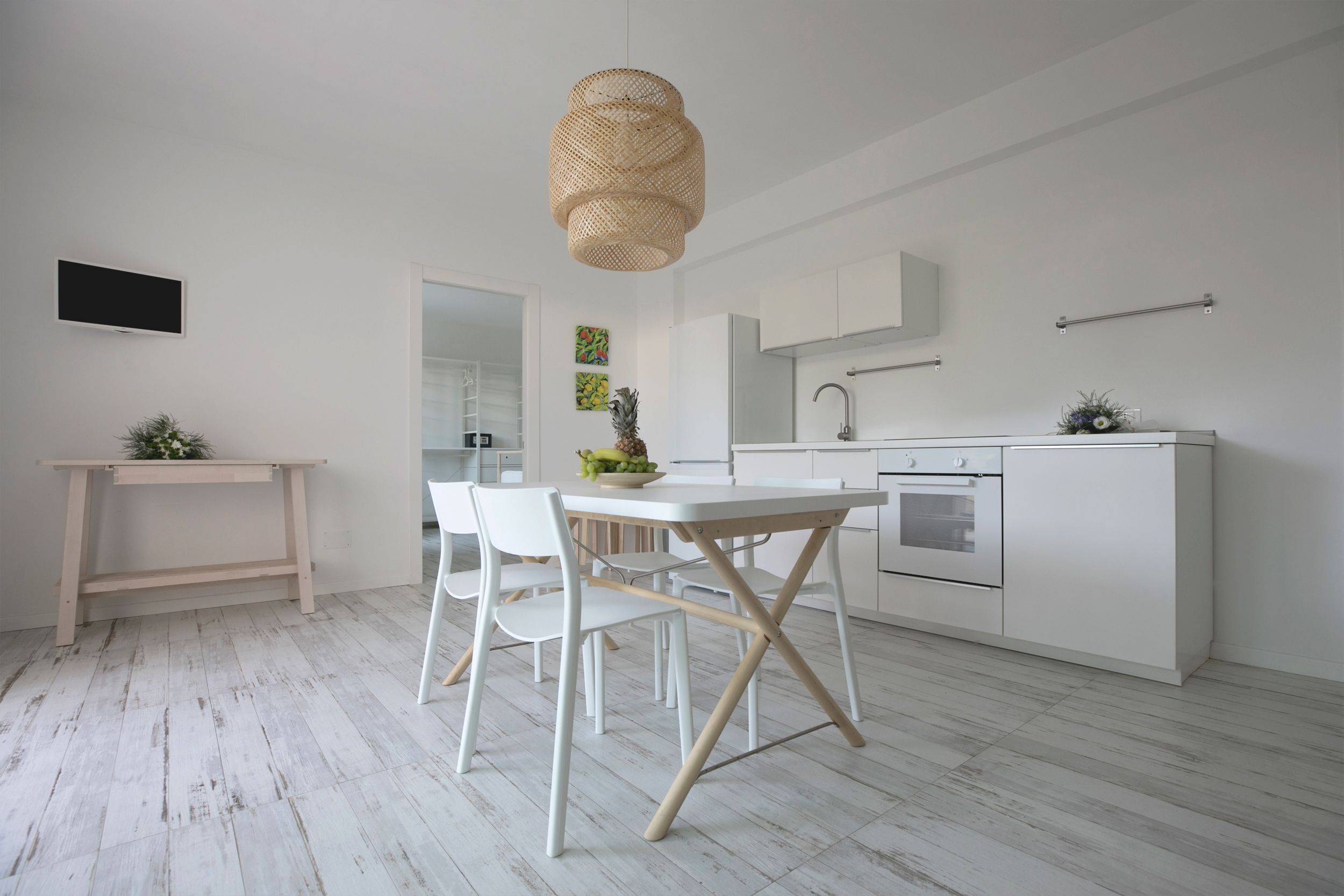 Une cuisine moderne avec des meubles blancs, une table à manger avec des chaises, un luminaire suspendu et une petite plante posée sur le comptoir.