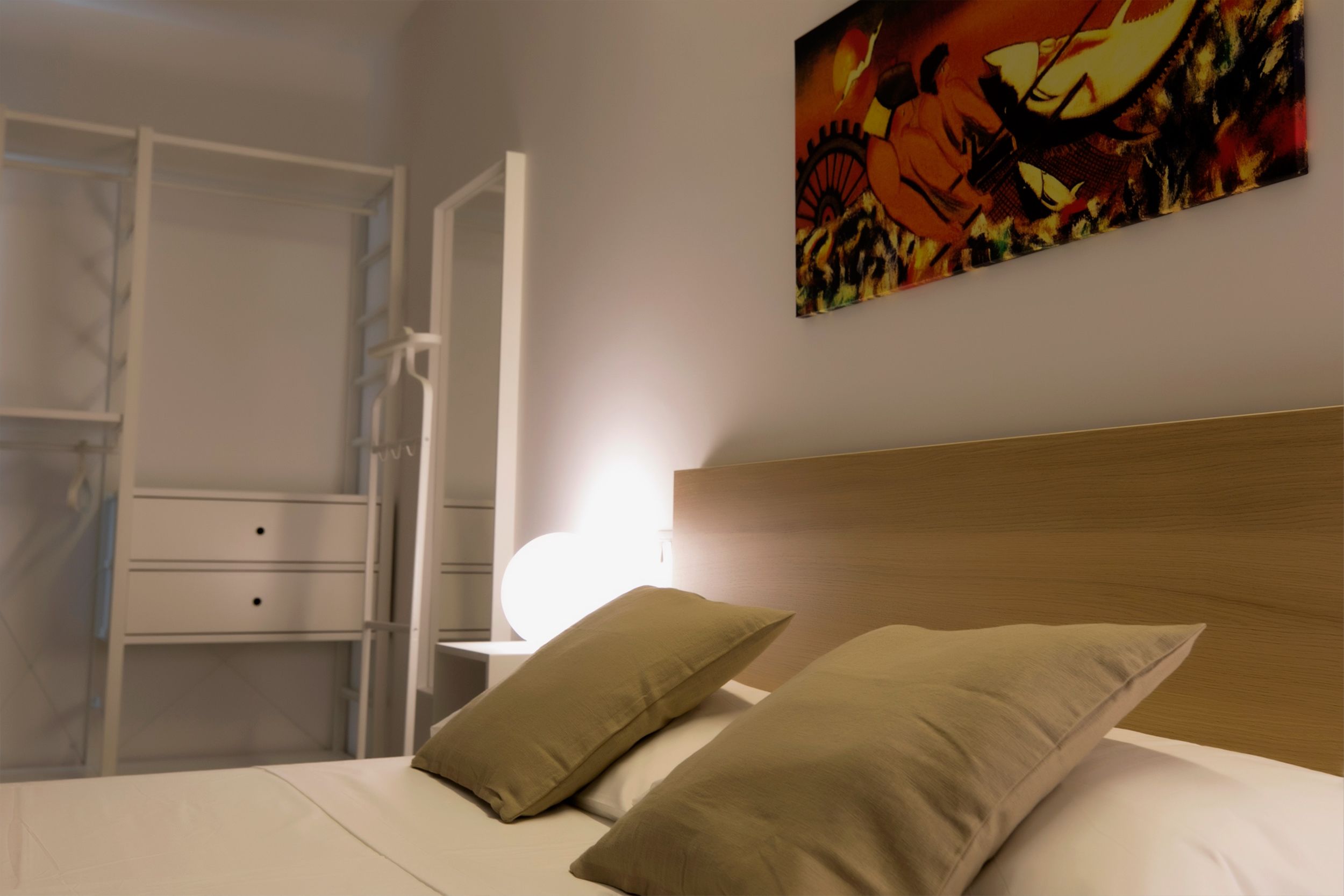 A bedroom with a bed, two pillows, a nightstand, a lamp, and a wardrobe.