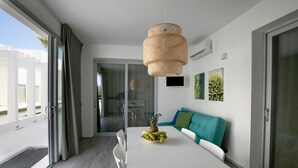 A modern dining area with a white table, a woven pendant light, and a teal sofa with green cushions. - Camarò Favignana (Favignana)